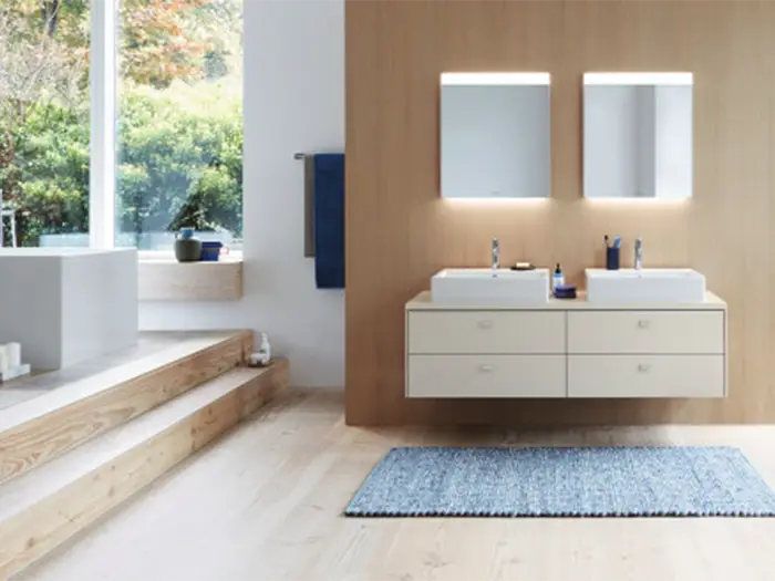 Moderner Doppelwaschtisch mit beleuchteten Spiegelschränken in hellem Badezimmer mit Holzwand.